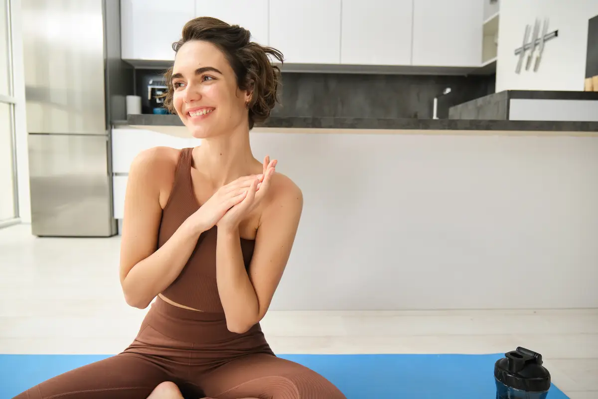 Happy and relaxed fitness girl sitting on rubber mat doing yoga meditating at home doing mindfulness