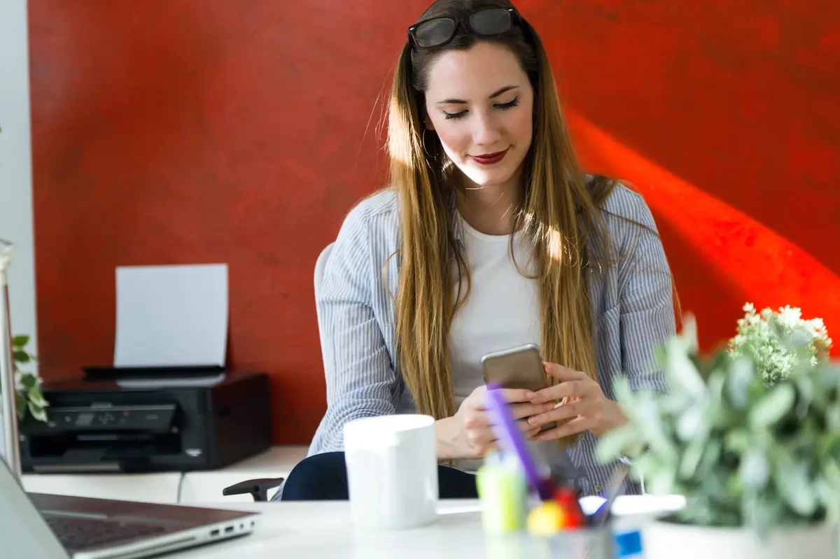 Beautiful young woman using her mobile phone in the office.