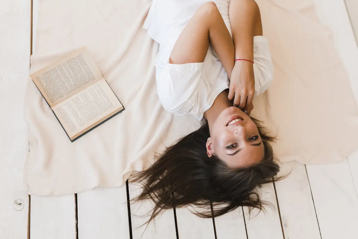 Woman lying near book and looking at camera