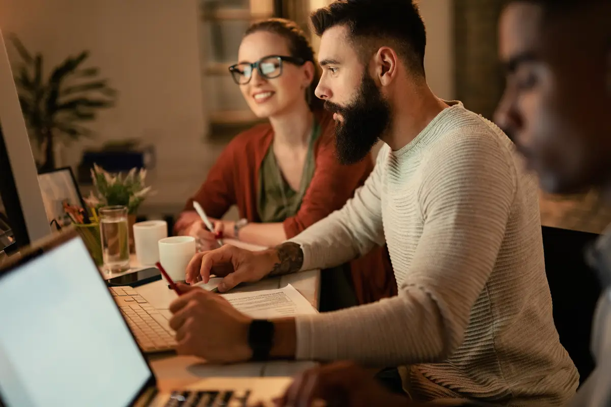 Young businessman working on desktop PC while being with his coworkers in the office