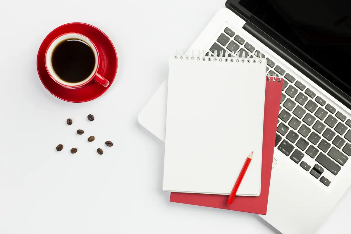 Coffee cup,coffee beans with spiral notepad on an open laptop against white background