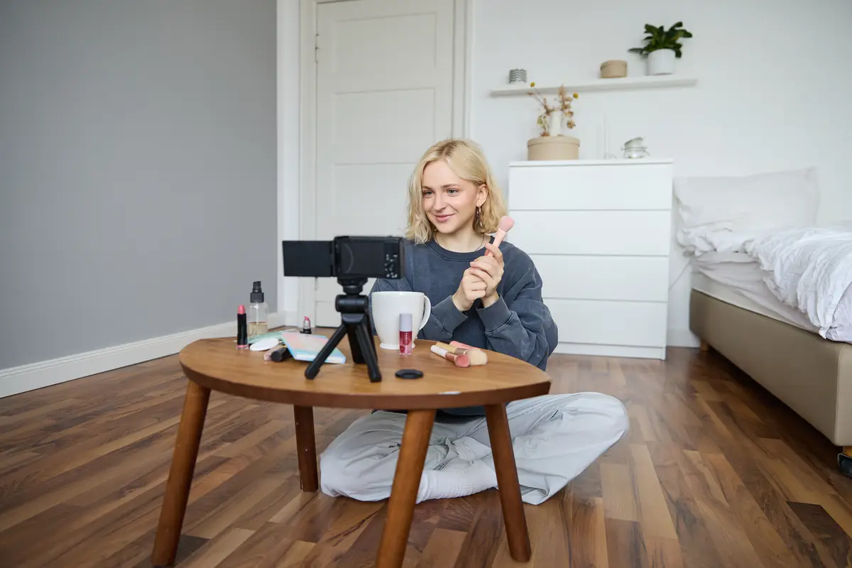 Portrait of beautiful smiling woman recording video in her room has camera on coffee table reviewing
