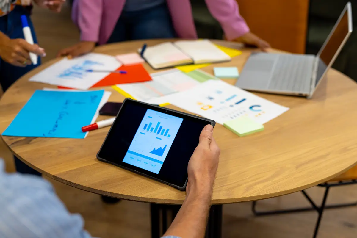 Midsection of diverse creative colleagues brainstorming with notes, tablet and laptop in meeting