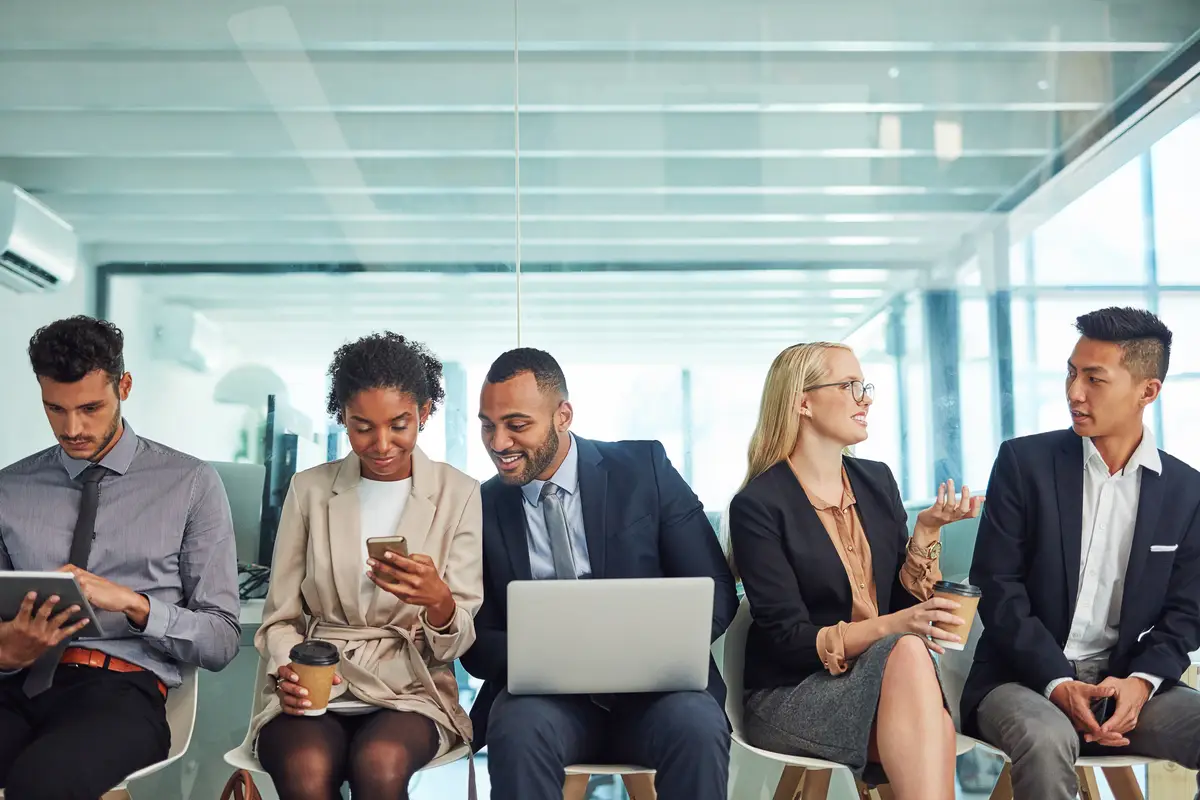 What a friendly environment to work in Shot of a group of focussed young businesspeople seated together on chairs and making notes using different methods while waiting in the office during the day