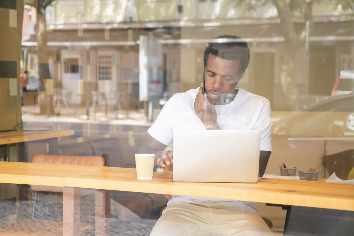 Serious African American man typing on laptop and speaking on cellphone in co-working space