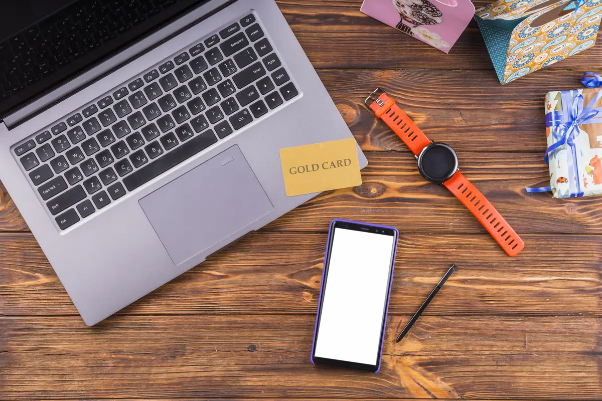 High angle view of laptop; cellphone; gift; and gold card on wooden desk