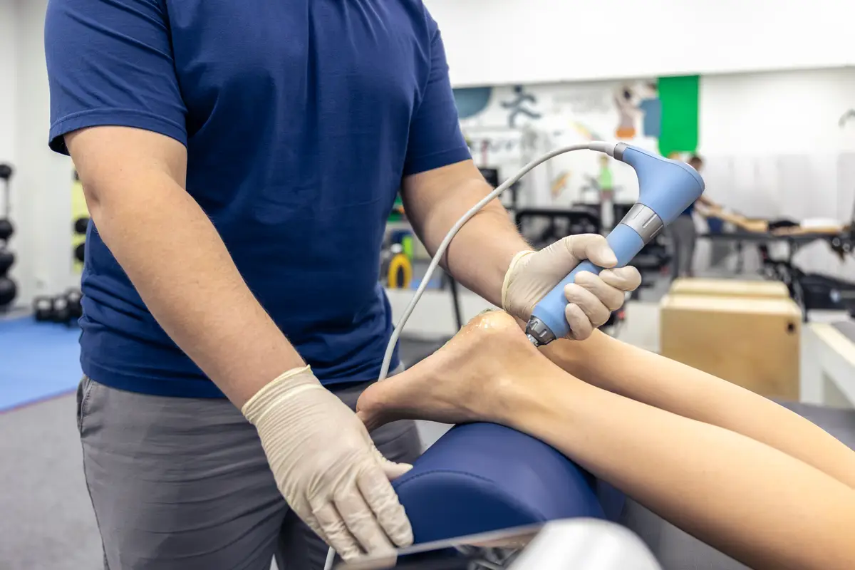 Physiotherapist treats patient foot with a rehab device leg rehabilitation session