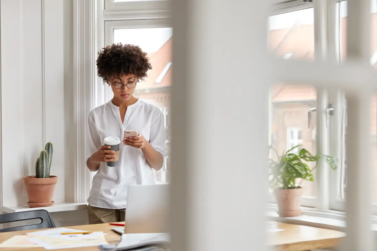 Busy black successful businesswoman or entrepreneur checks notification on mobile phone, drinks takeaway coffee