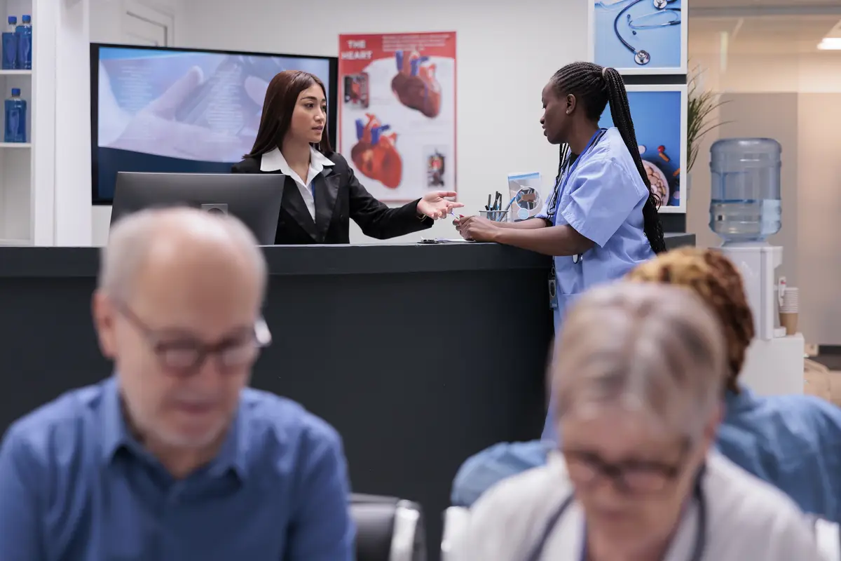 Diverse medical staff working at reception counter, filling in checkup report papers and making appointments. Nurse and receptionist doing registration work in hospital waiting room.