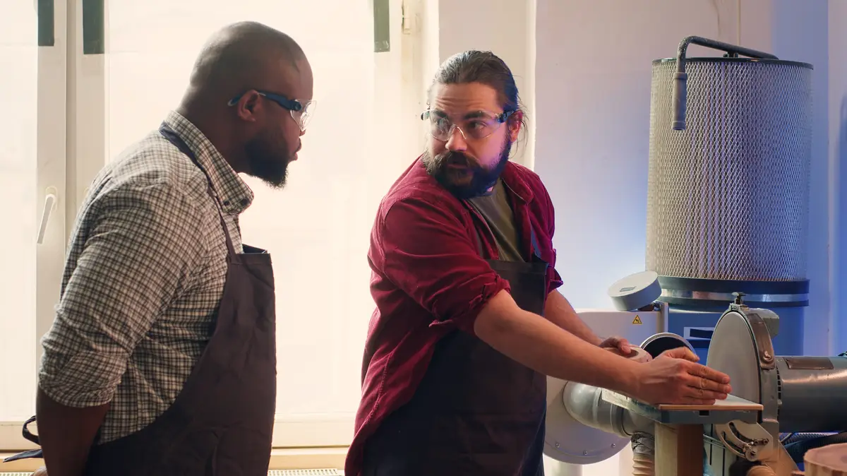Manufacturer teaching new employee how to shape wooden bowl on disc sander