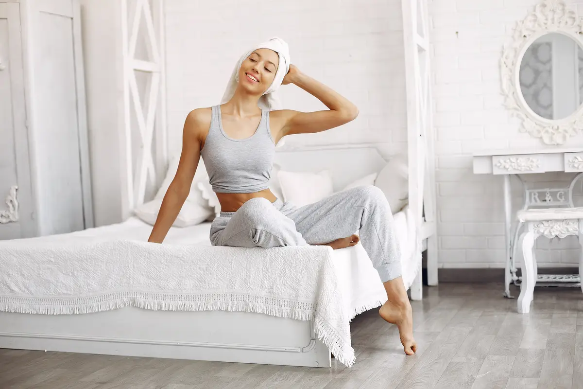 Beautiful girl sitting on a bed with beauty products