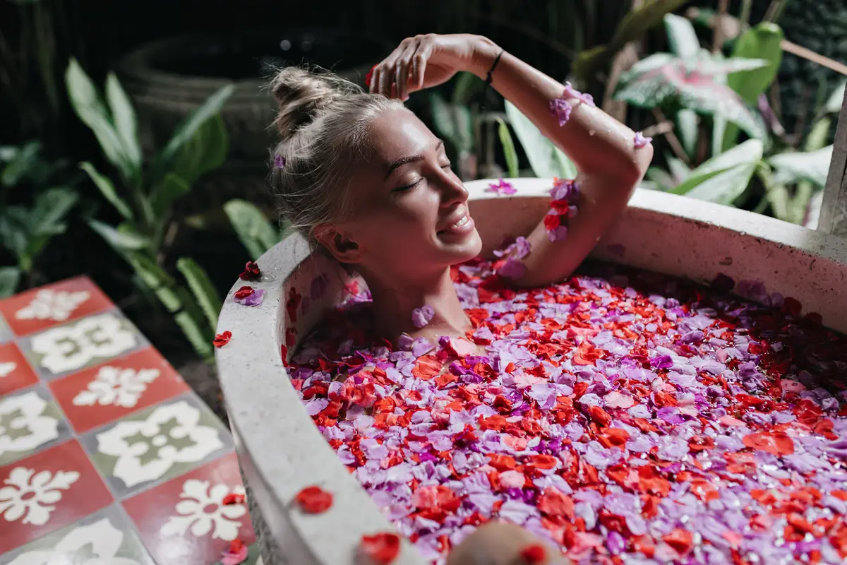 fair-haired girl smiling while chilling in bath. Gorgeous caucasian woman having fun during spa with flowers.