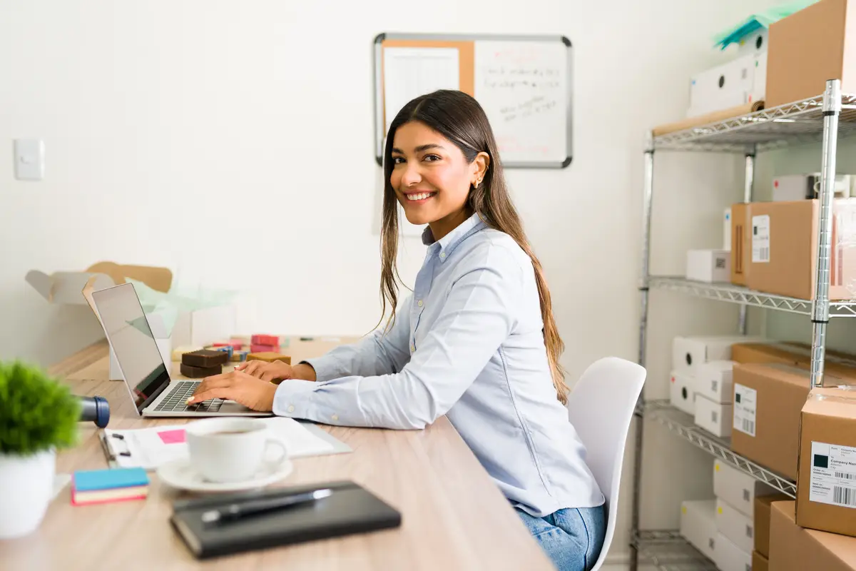 Beautiful business owner smiling and making eye contact while working at her office desk of her online startup company