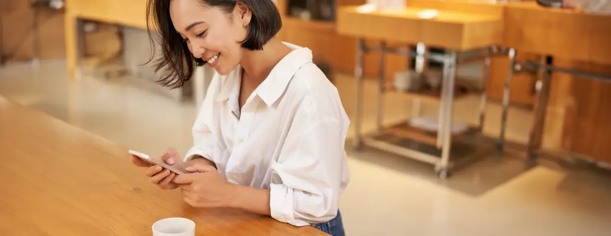 Portrait of young asian woman sitting in cafe holding smartphone chatting and messaging while
