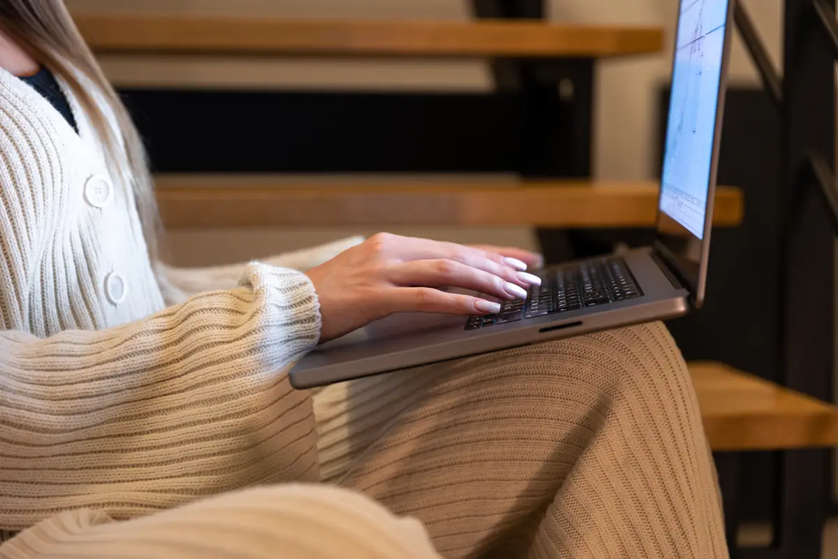 Woman typing on laptop on home stairs warm work evening