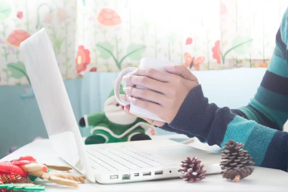 Hands holding cup of coffee and using laptop with Christmas decoration, Shopping online