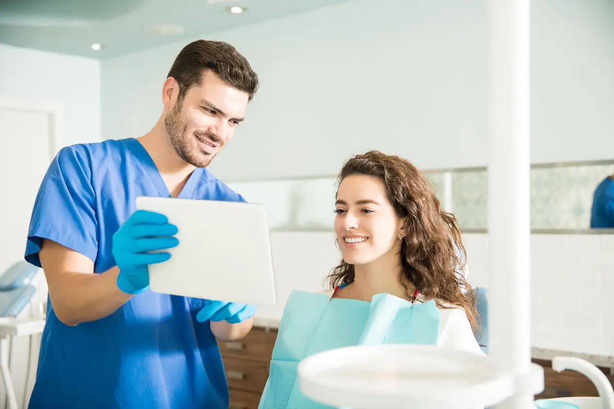 Mid adult dentist showing digital tablet to female patient during treatment in dental clinic