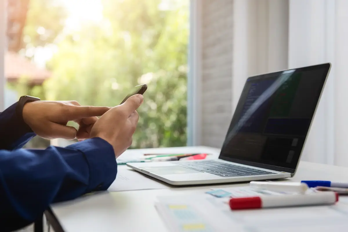 Cropped hands of software developer using mobile phone on table