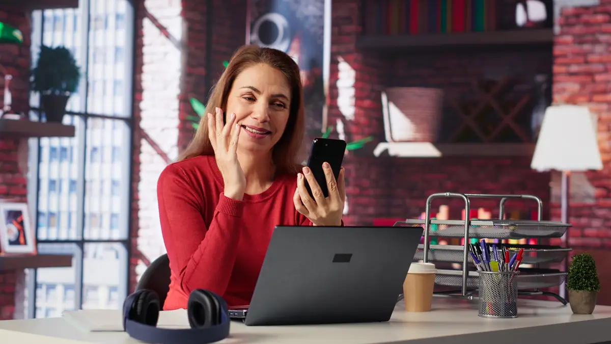 Mature adult smiling and waving during a video call at home desk