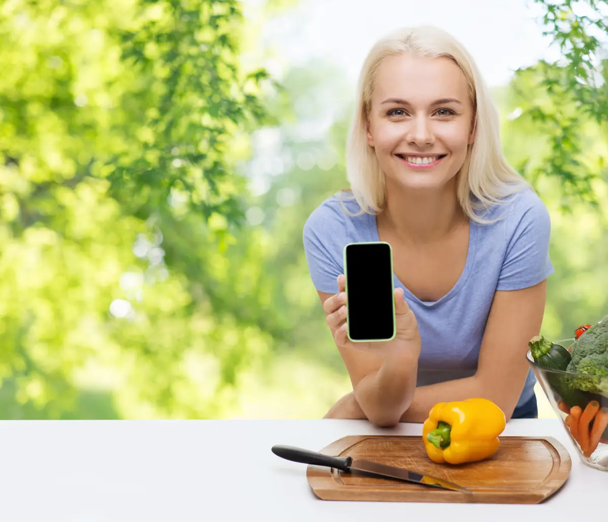 smiling woman with smartphone cooking vegetables