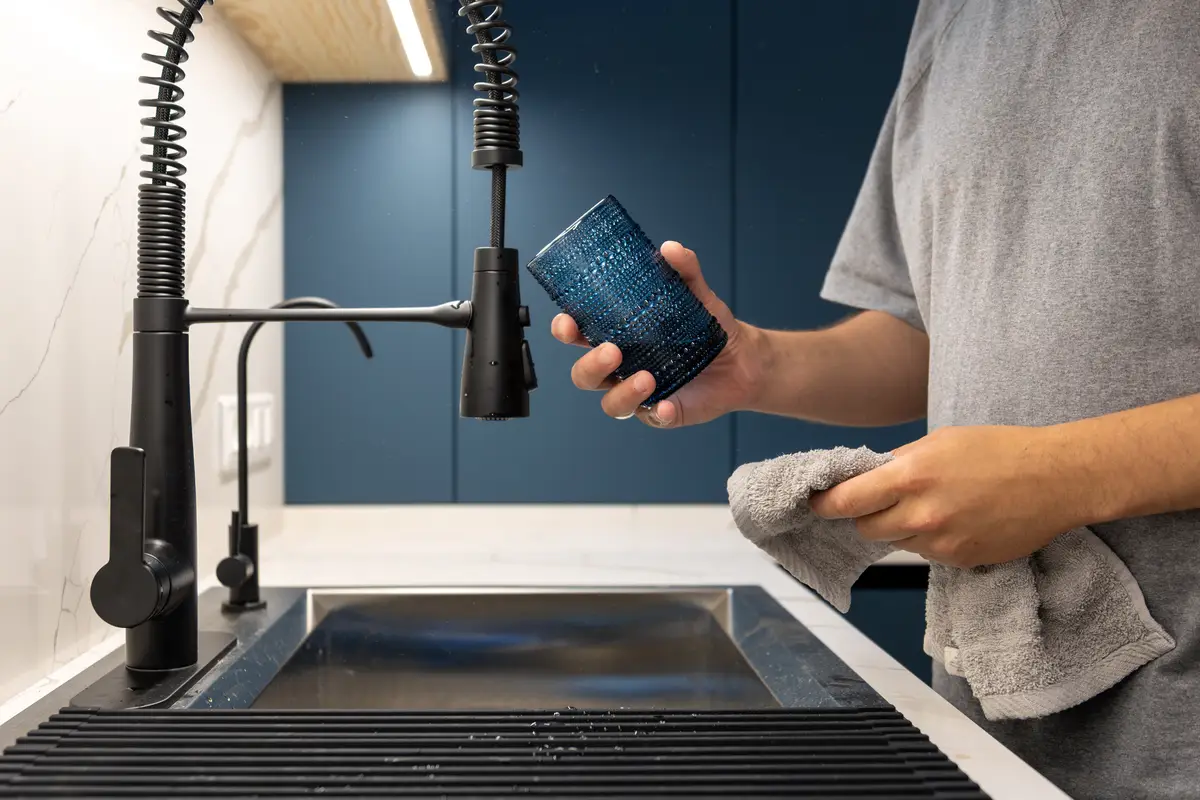 Man holding wet glass by faucet and towel polishing glass