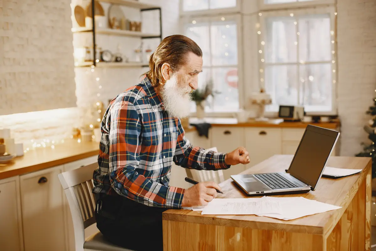 Old man with laptop. Grandfather sitting in a Christmas decorations. Man in a cell shirt.