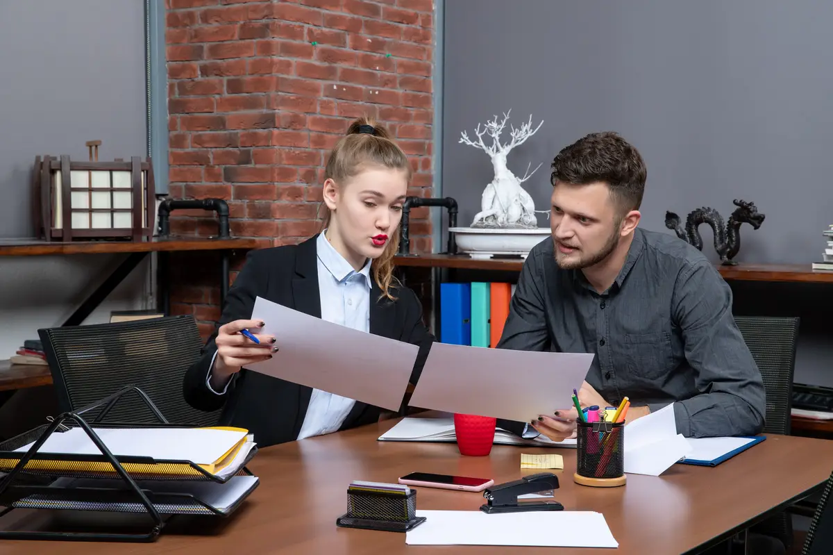 Top view of young busy and motivated clerical workers discussing one issue in the documents in the office