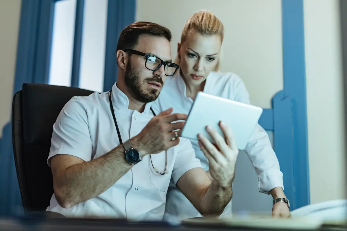Two healthcare workers analyzing medical records on touchpad while working at clinic