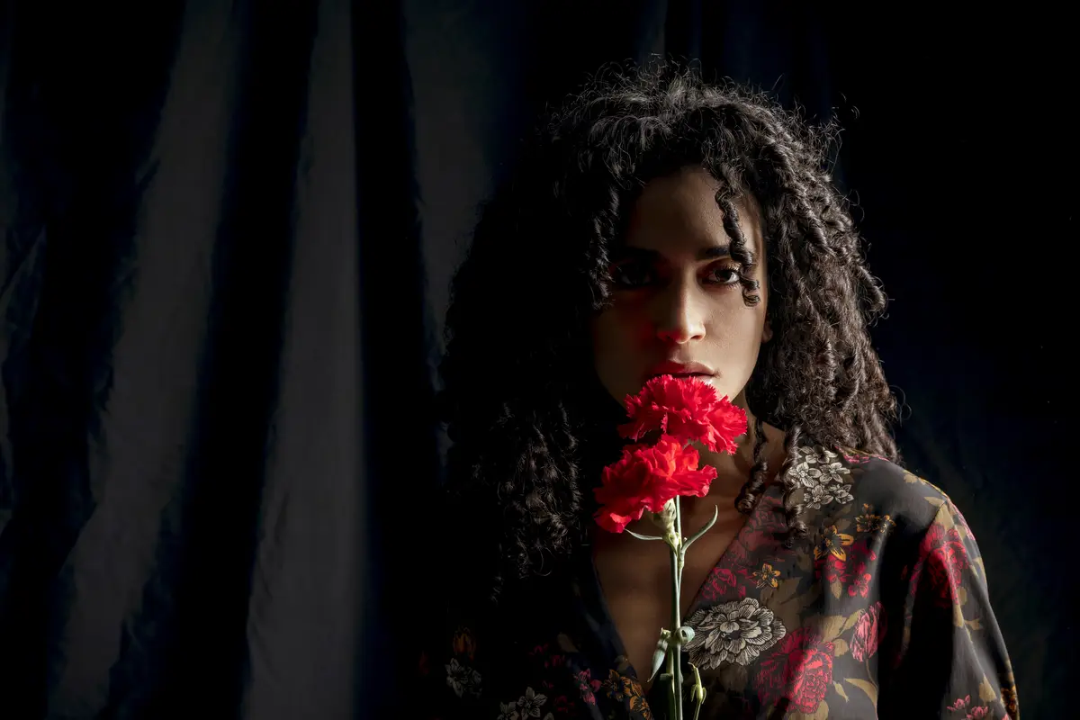 Seductive woman with red flowers in darkness