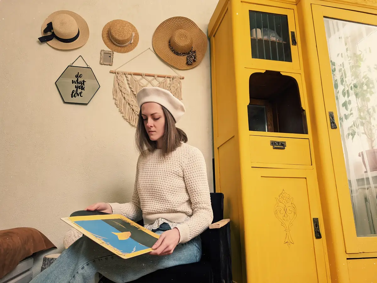 Young woman in beret sits in cozy home room with music record in hands vintage yellow cabinet