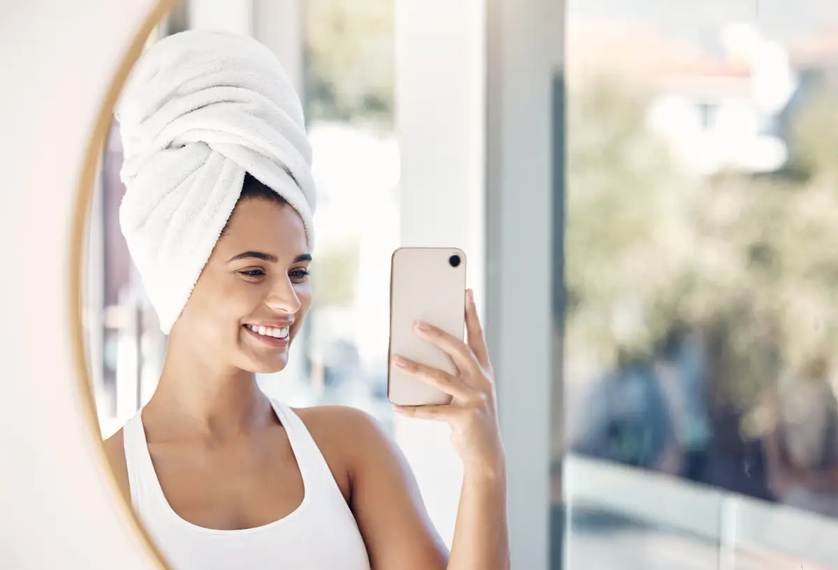 Portrait phone selfie and woman towel and bathroom for skincare beauty and cleaning in mirror reflection Face girl and smile for picture after facial treatment grooming and hygiene with a smile