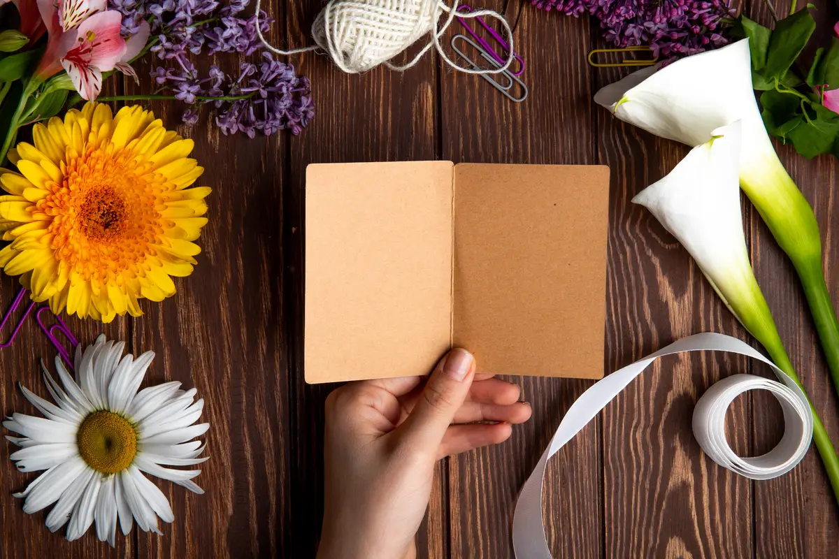 Top view of a hand with a postcard and gerbera with daisy flowers on wooden background