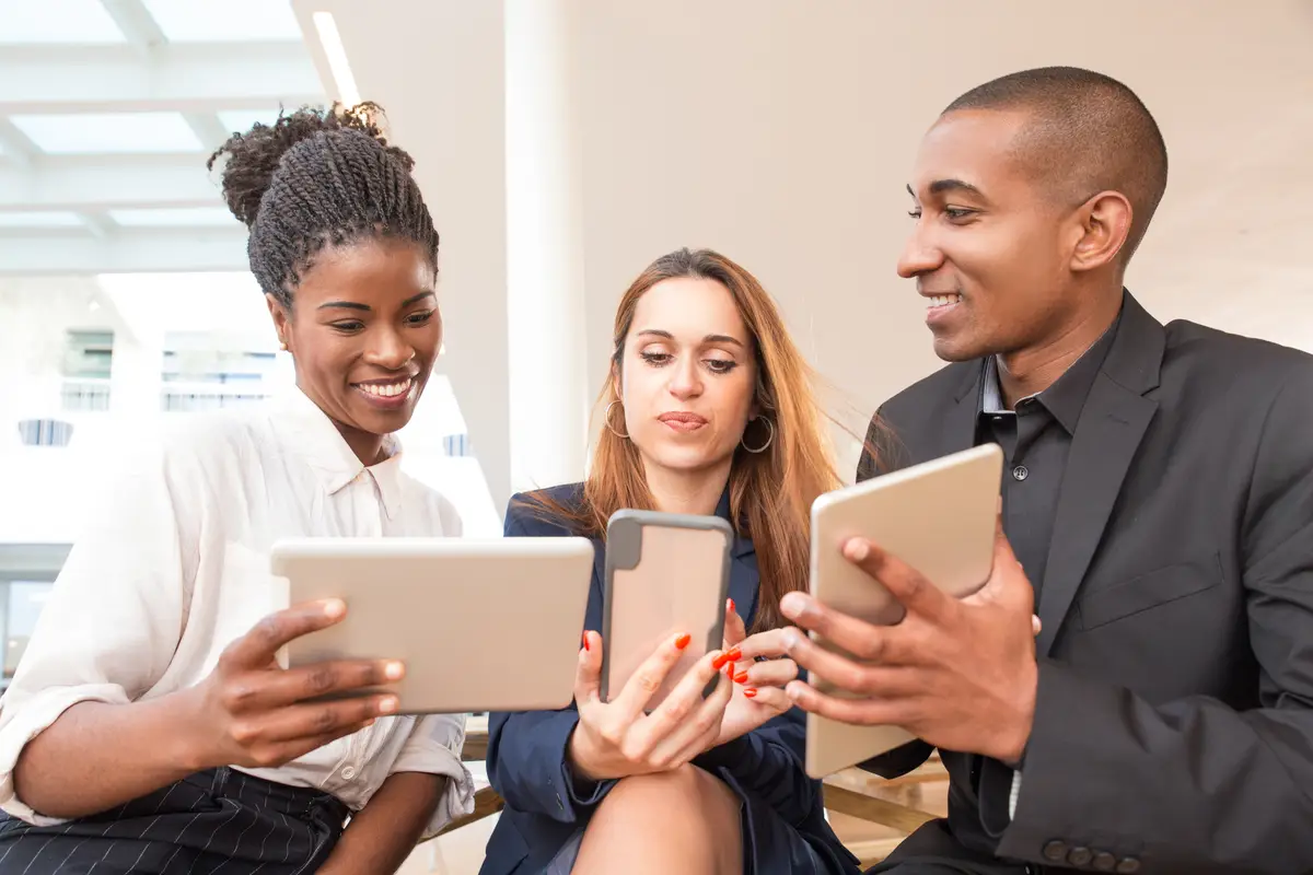 Three happy businesspeople using gadgets in office