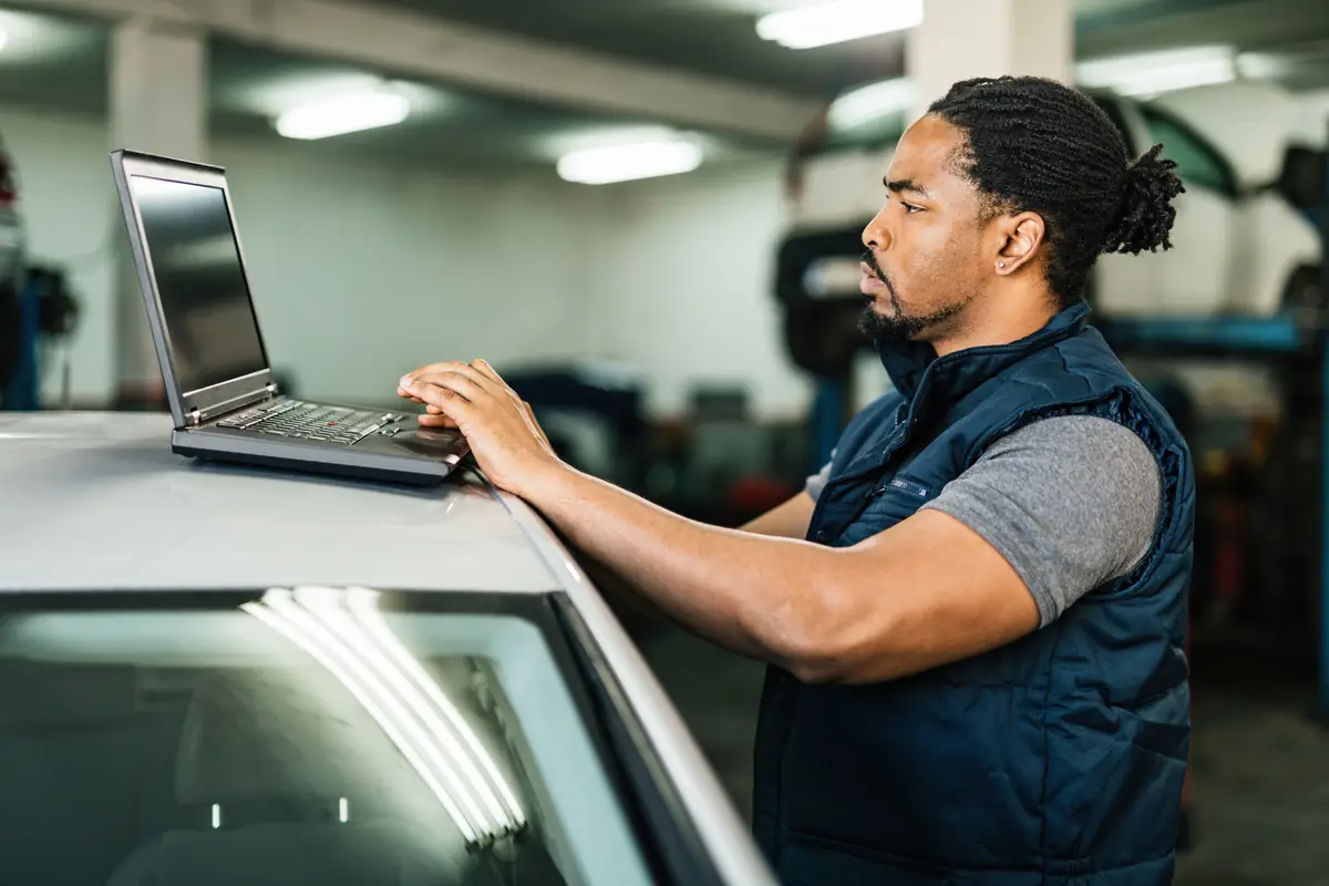 Young African American car mechanic using laptop in repair workshop