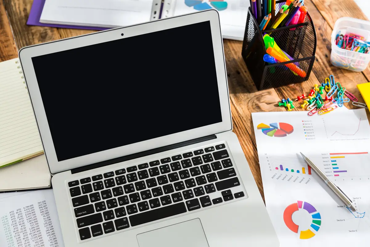 Laptop with pie charts next to it and other papers