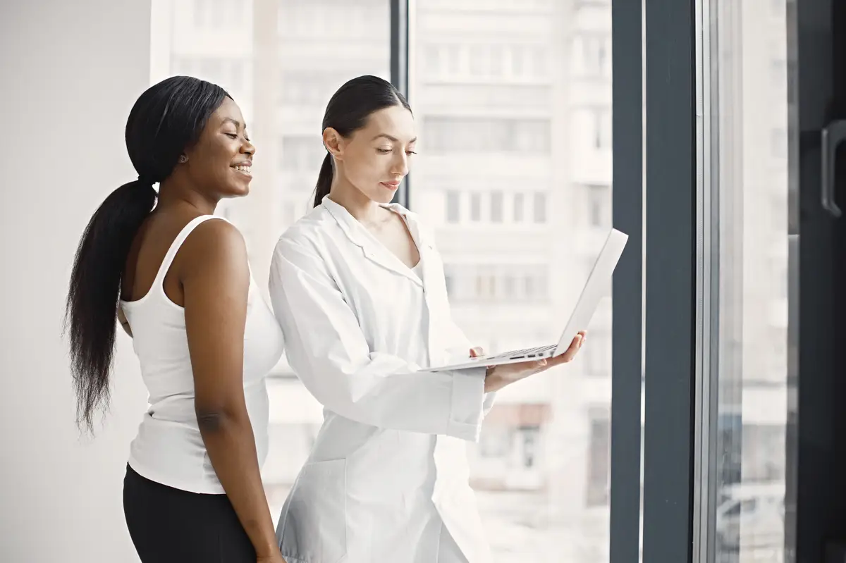 Portrait of female caucasian doctor and black patient standing in office at clinic