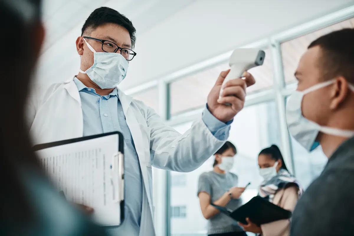 Doctor testing covid temperate in hospital appointment to prevent the spread of the virus Healthcare compliance worker with health insurance document and face mask checking or scanning patient head