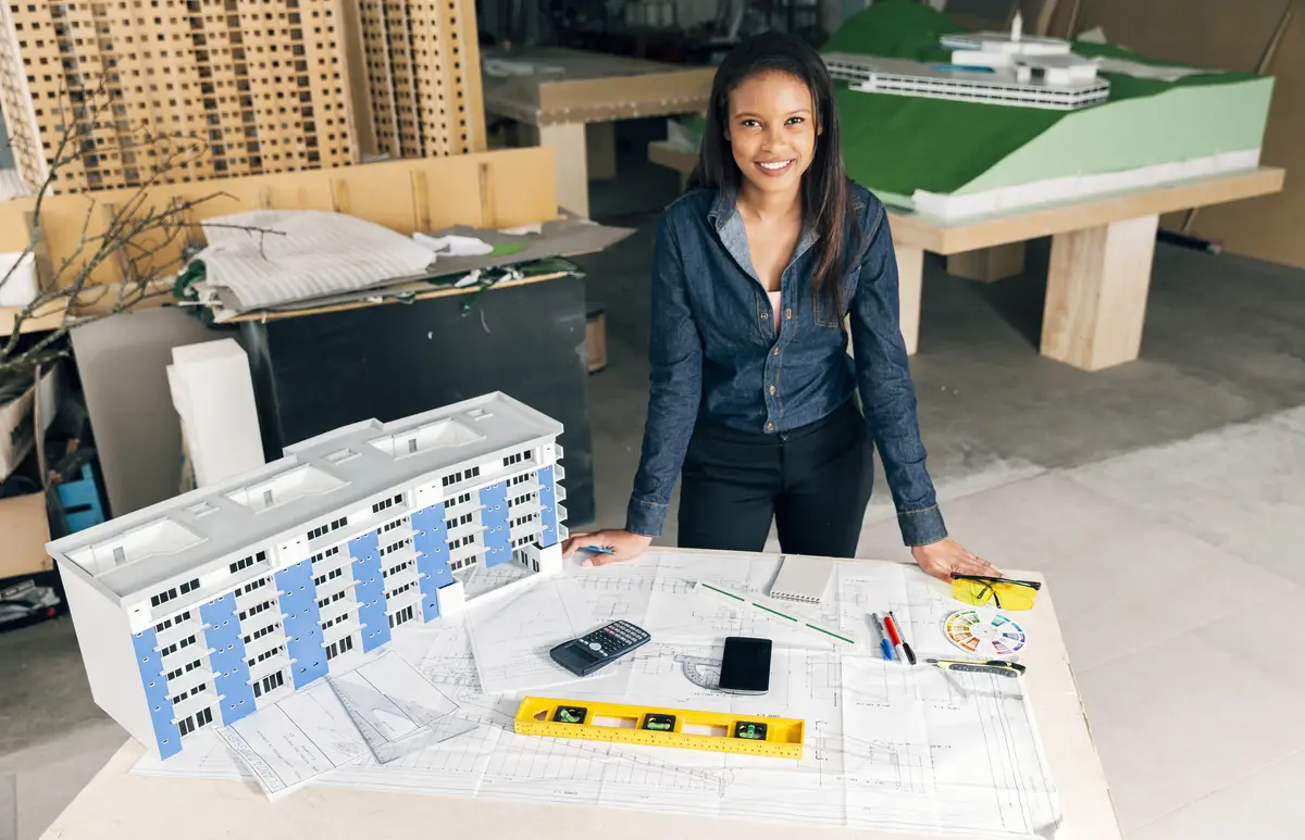 Happy African-American lady standing near model of building on table