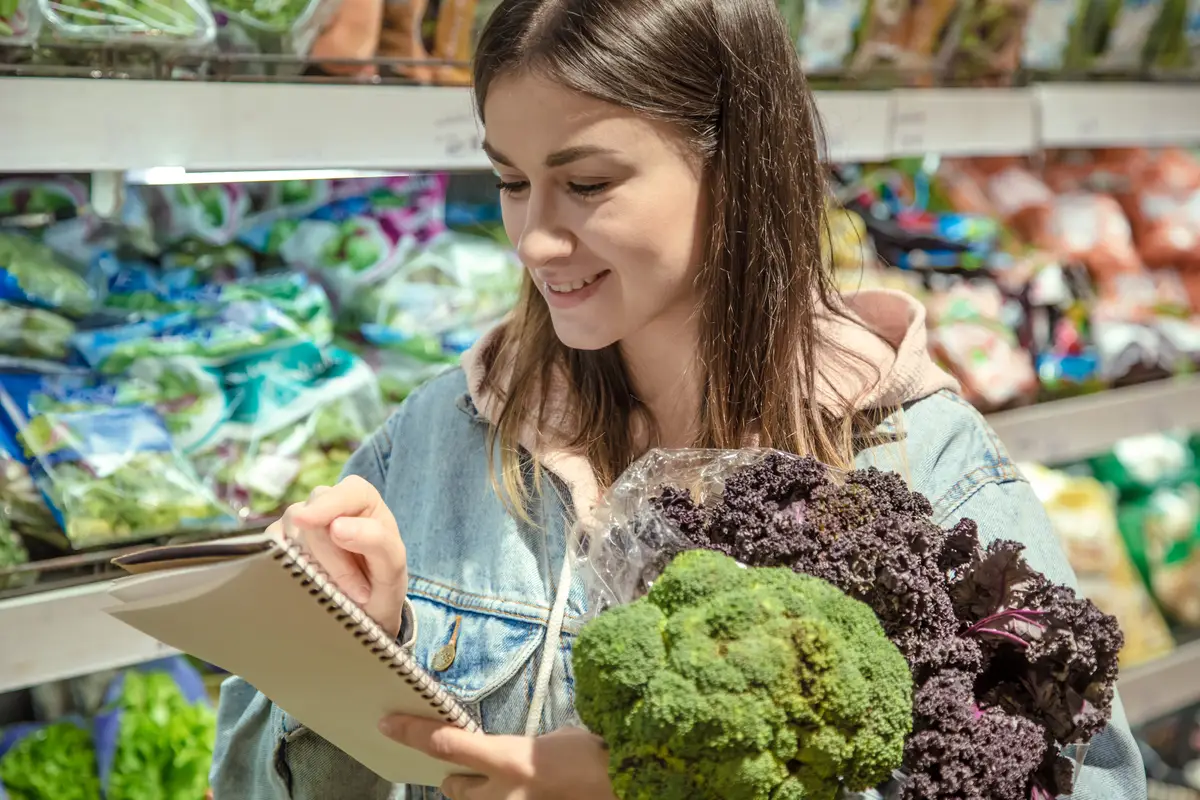 A young woman with a notebook buys groceries in the supermarket.