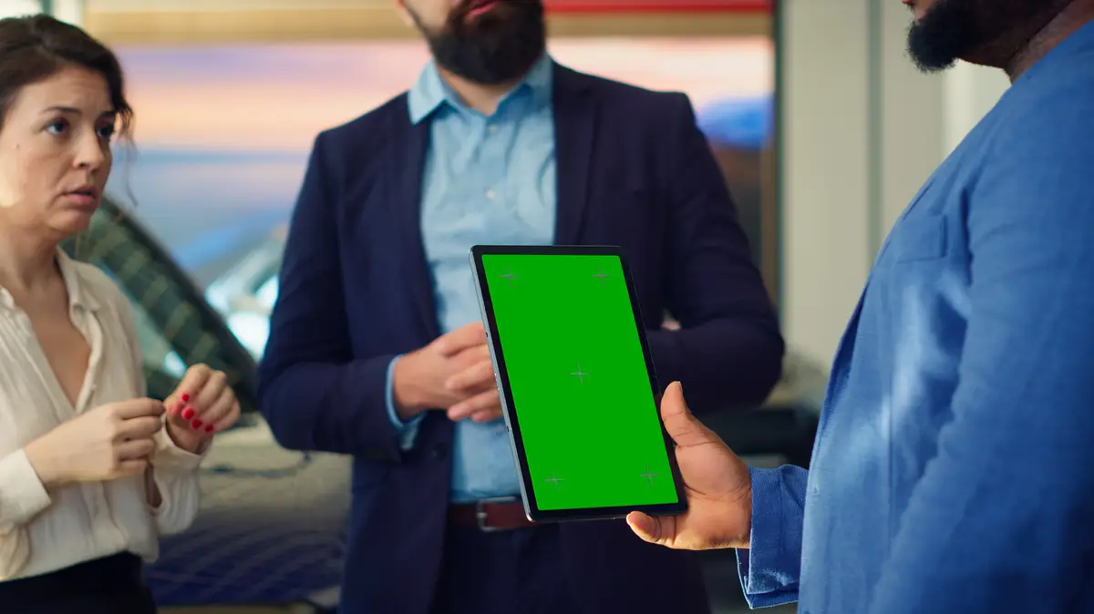 Dealership salesman showing car models on green screen tablet to clients