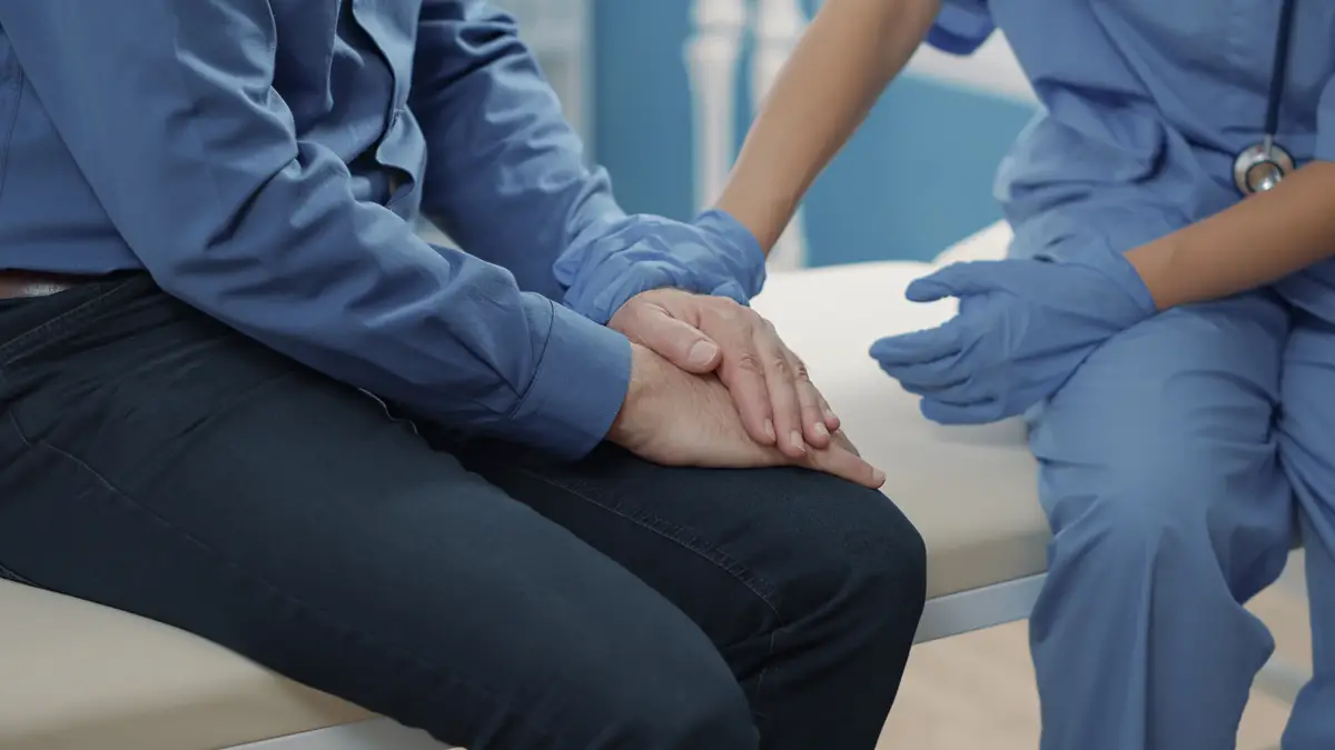 Medical assistant comforting senior patient to help with recovery, showing compassion after finding out health care diagnosis. Nurse giving support after sharing disease news. Close up.