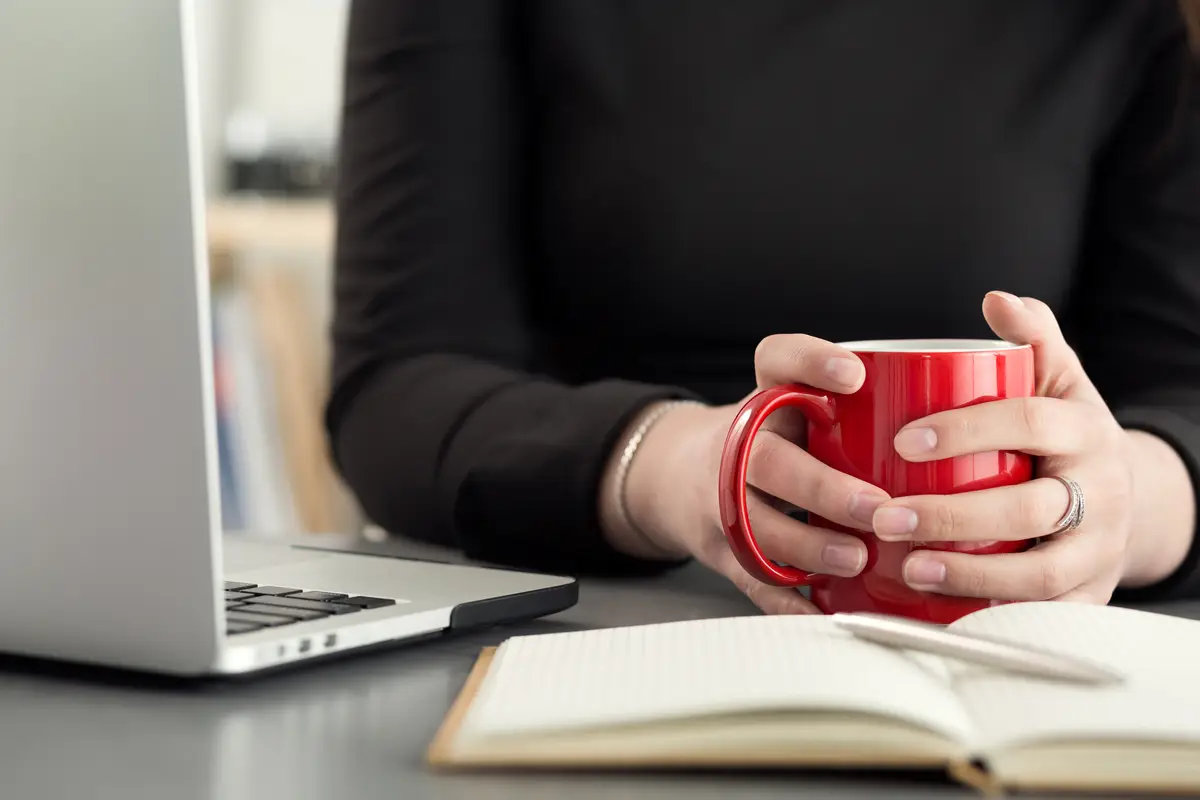 Female designer in office drinking morning tea or coffee. Coffeebreak during hard working day. Girl holding cup of hot beverage.
