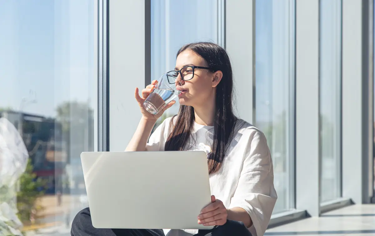 Young woman with a glass of water in front of a laptop in the morning
