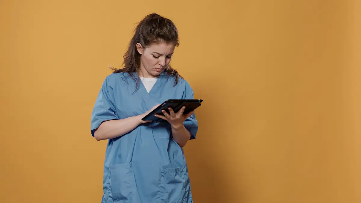 Portrait of woman doctor holding tablet typing patient data wearing hospital uniform standing in studio. Professional medic using digital touchscreen modern technology for health care concept.