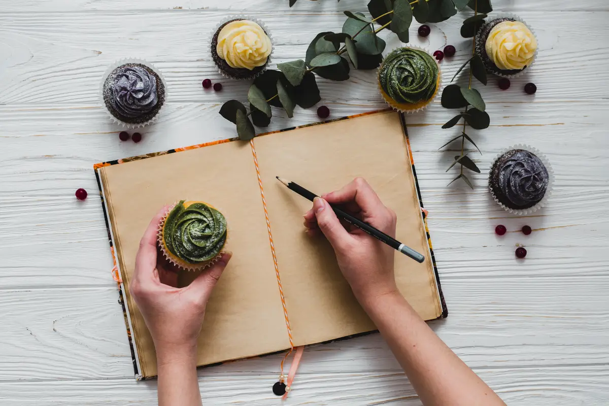 Crop person with cupcake writing in notebook