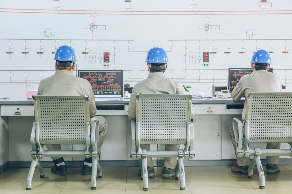 Trabalhadores em sala de controle monitorando instalações elétricas industriais