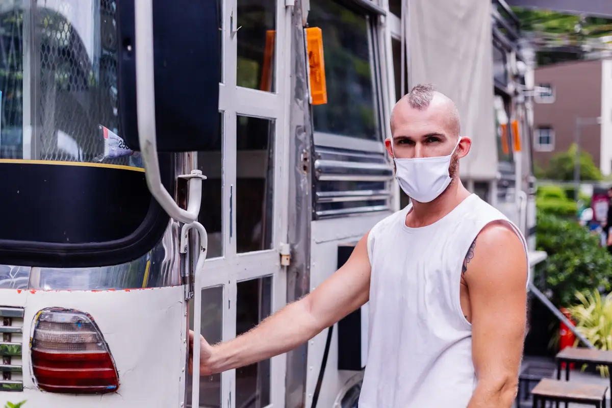 Portrait of man in white medical mask on central square in city sits on chair in van cafe
