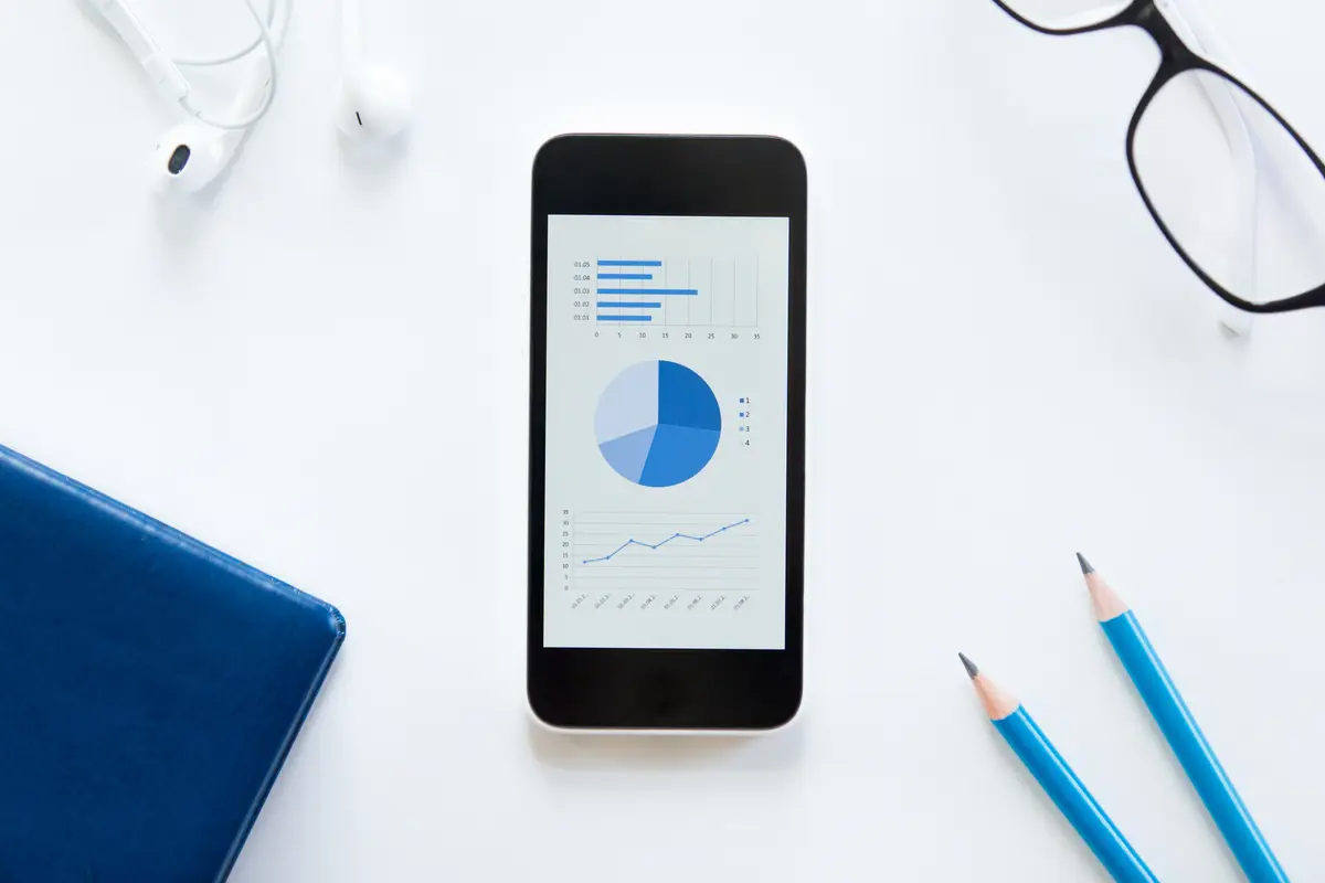 White desk with glasses, phone with a diagram, earphones
