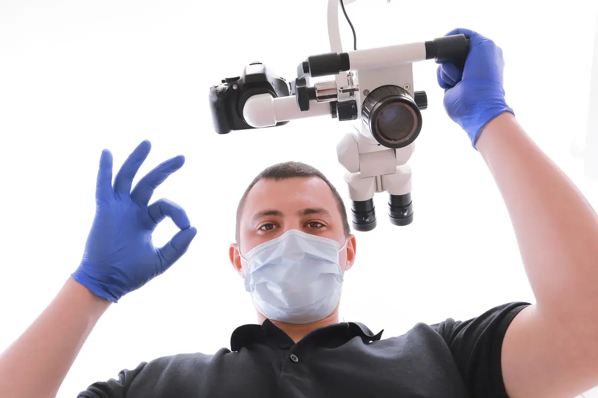 Male dentist in uniform, medical mask and glovers looking at camera and showing fingers ok.
