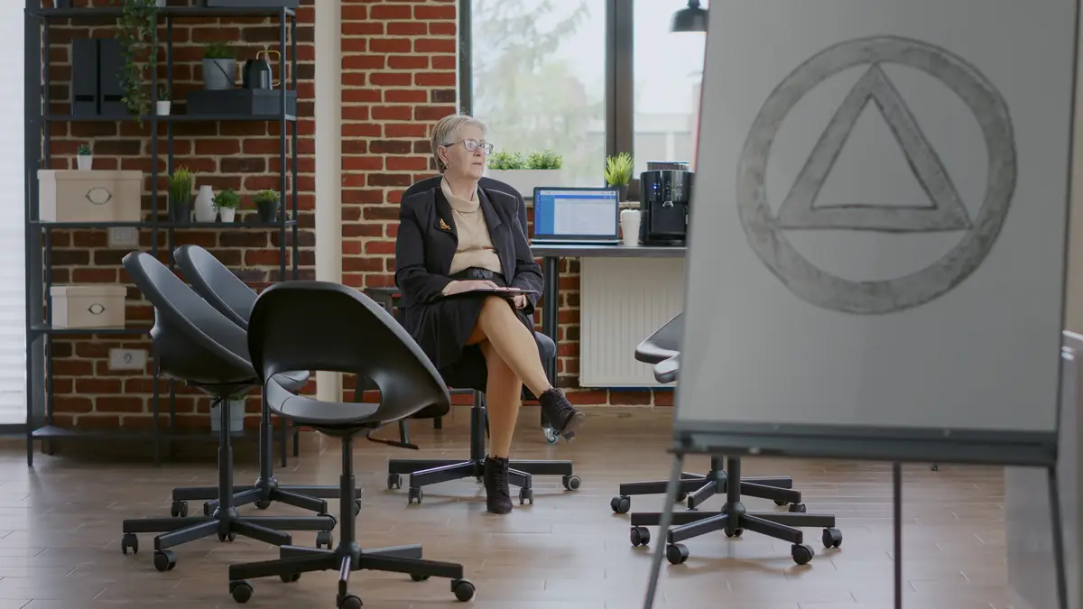 Woman psychiatrist waiting on people to attend aa group therapy meeting. Psychotherapist sitting in circle with chairs and holding clipboard to give advice to rehabilitation patients.